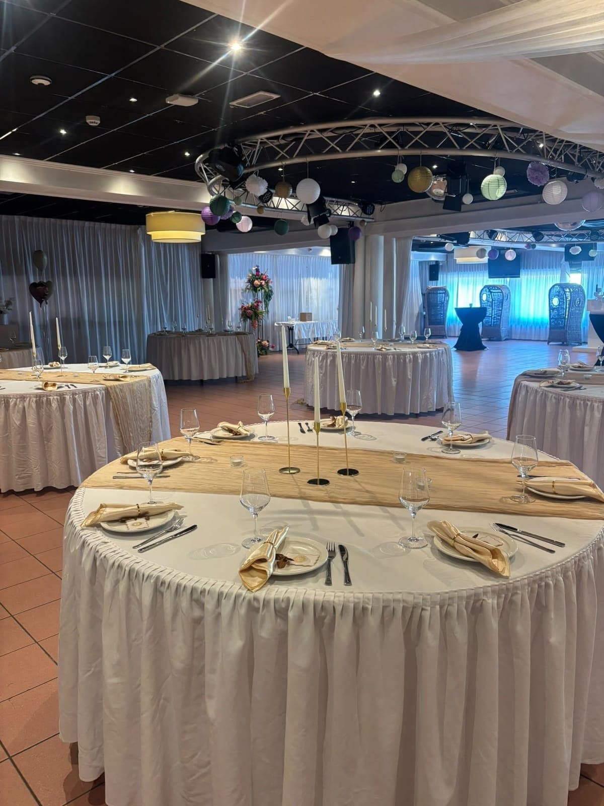 De South Beach Lounge gedekt voor een bruiloftsdiner, met ronde tafels in witte rokken, gouden lopers en kaarsen, en lampionnen aan een ronde truss