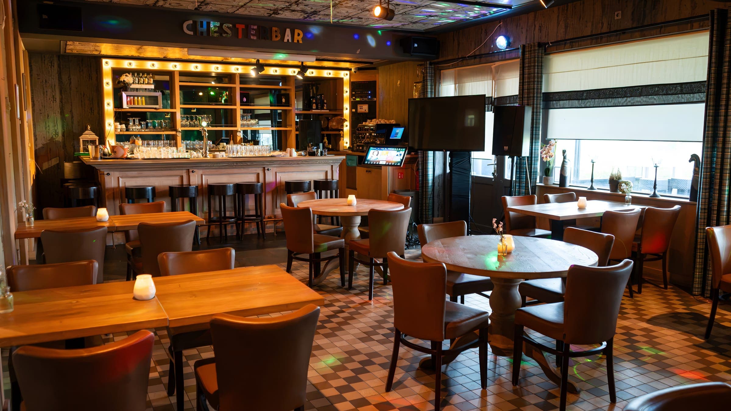 De Chesterbar: een bar met een lijst van lampjes, houten tafels met leren stoelen en een geblokte vloer