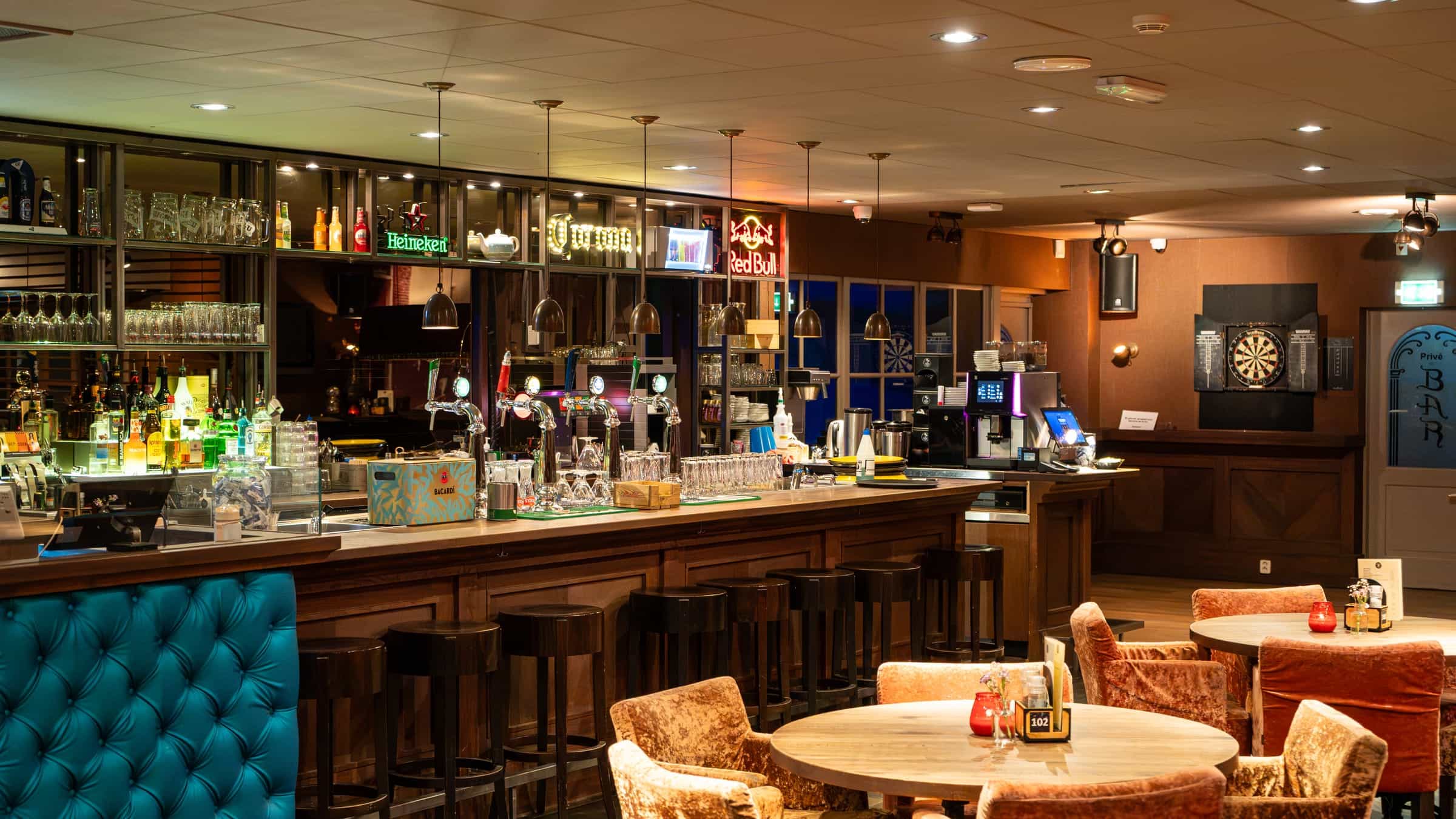 Het Grand Café van Bobs: de lange bar met krukken, ronde tafels met fluwelen stoelen en een turquoise bank