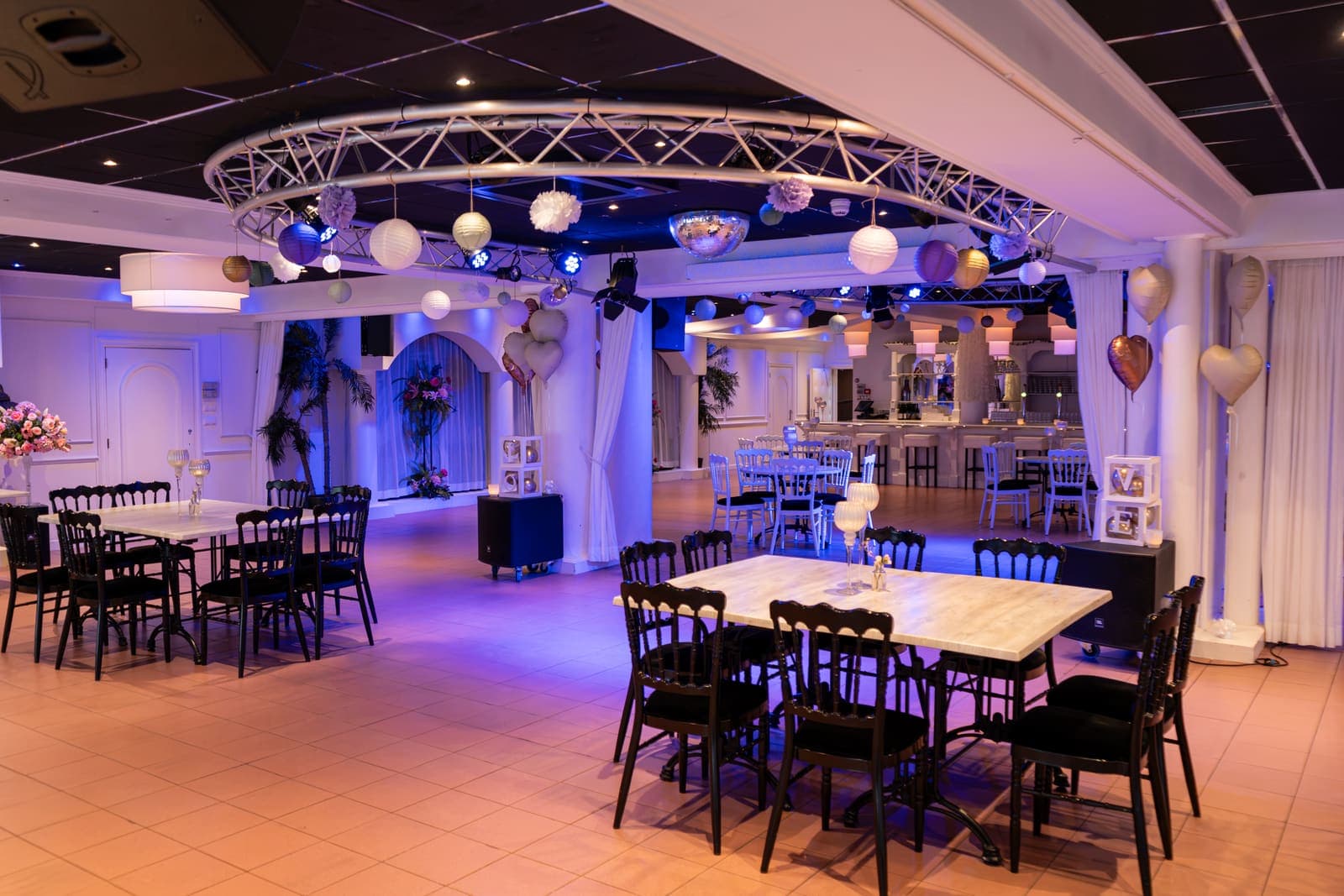 Lange tafels met zwarte stoelen in de South Beach Lounge, met bloemen tegen de witte gordijnen