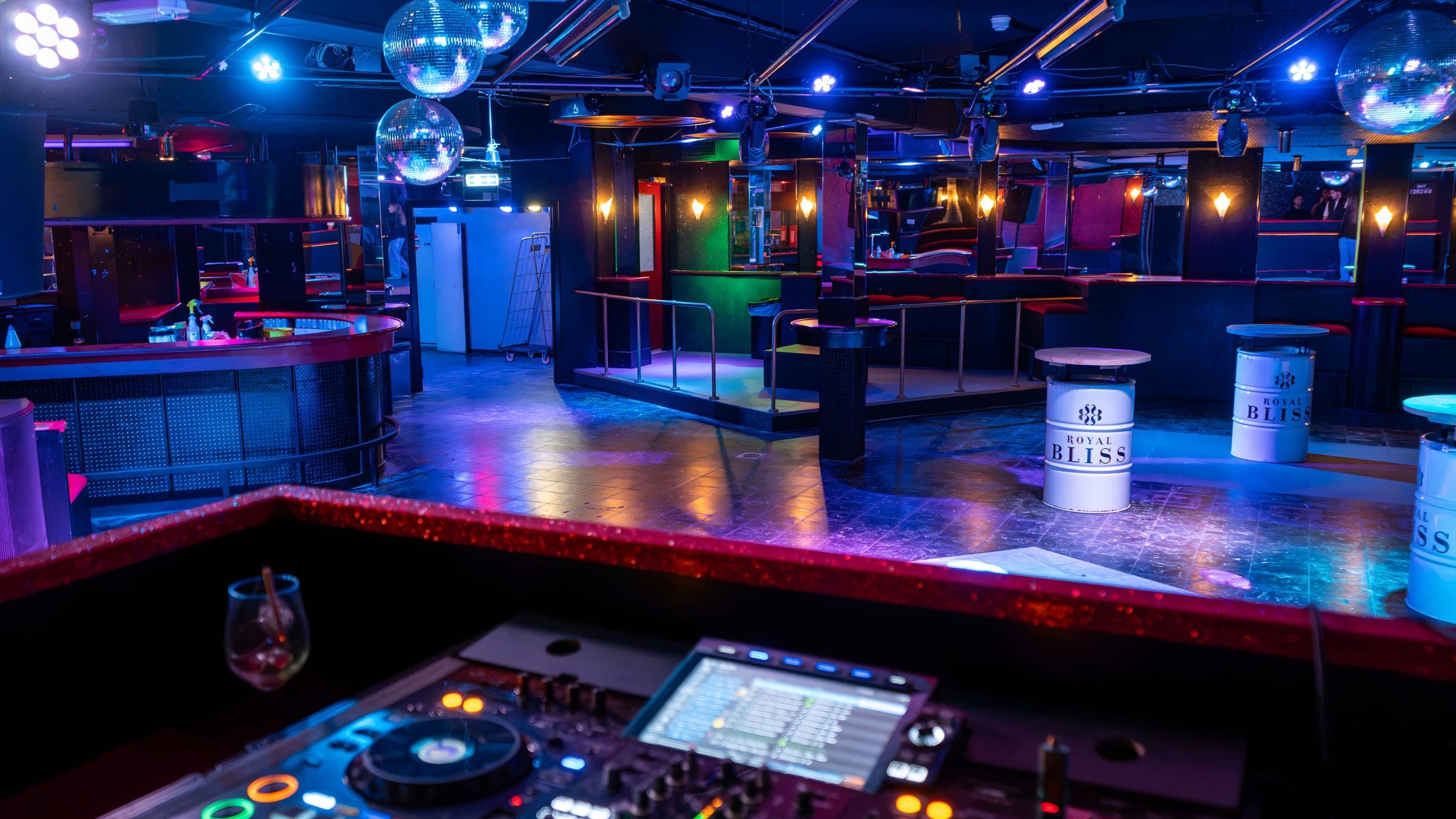 Turbo 2000 vanuit de DJ-booth: de mengtafel op de voorgrond, de dansvloer en de bar in blauw en paars licht met discobollen
