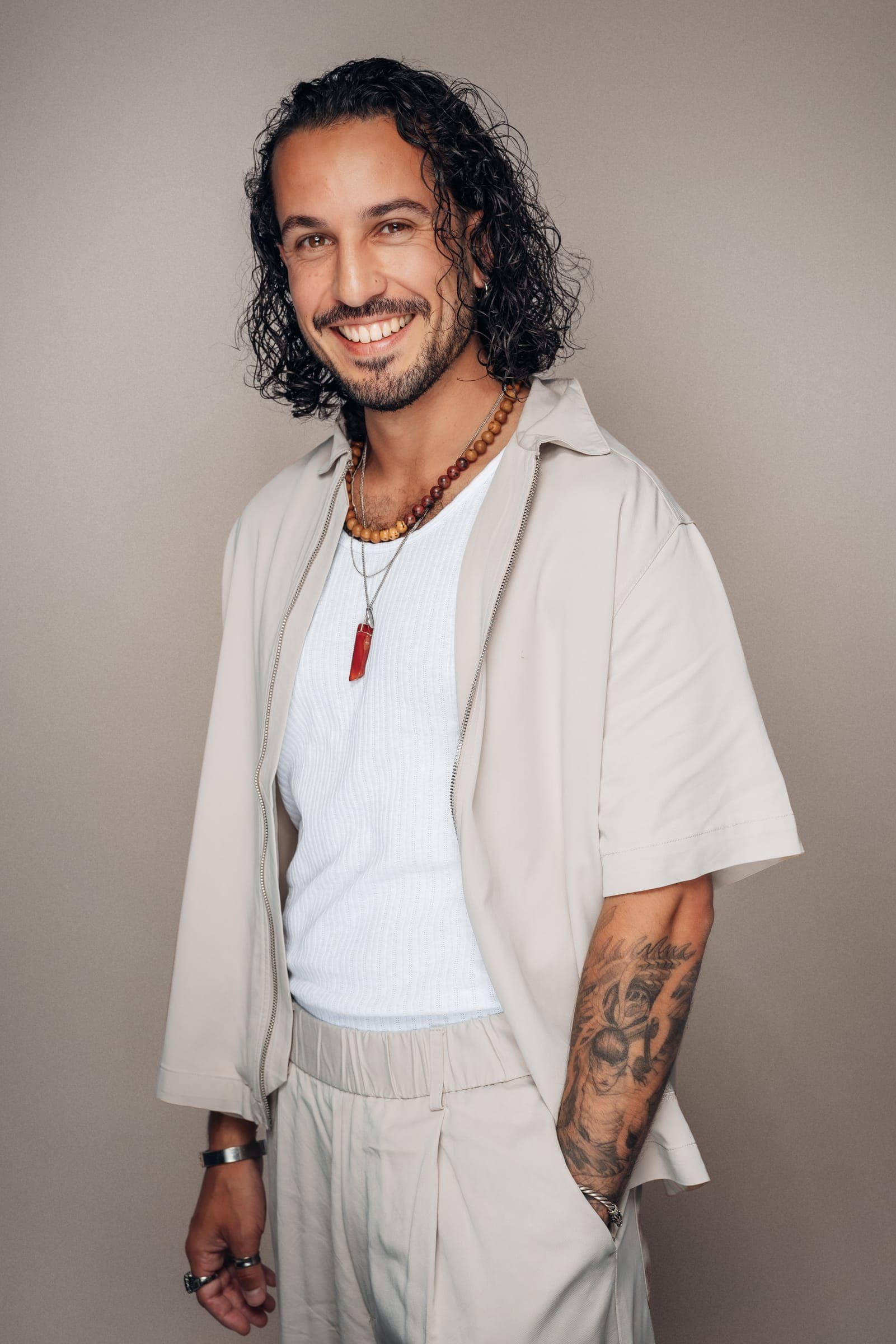 Jake Monteiro lachend in een wit overhemd en lichte jas