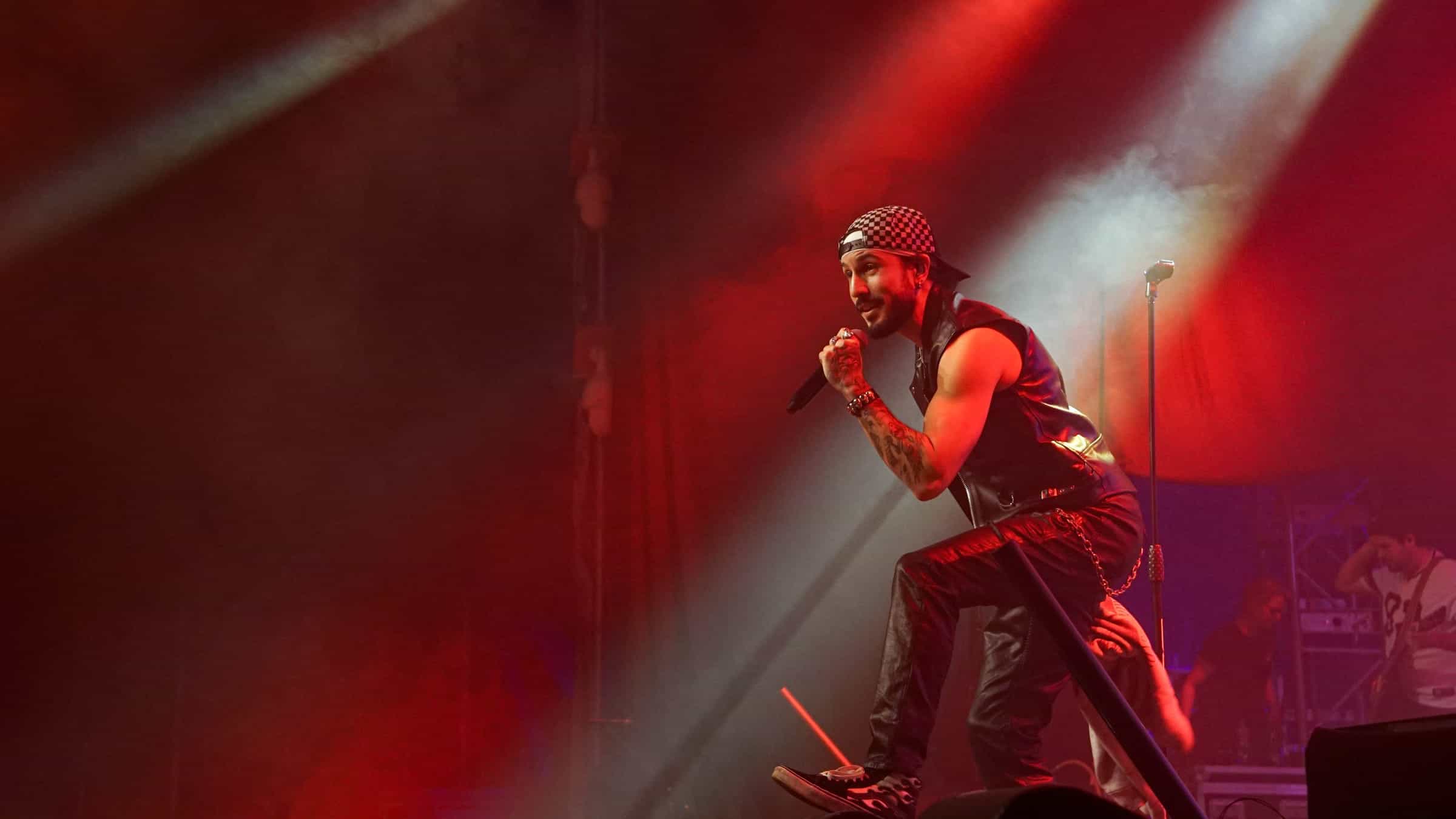Jake Monteiro zingt op een podium in rood licht, met de band achter hem