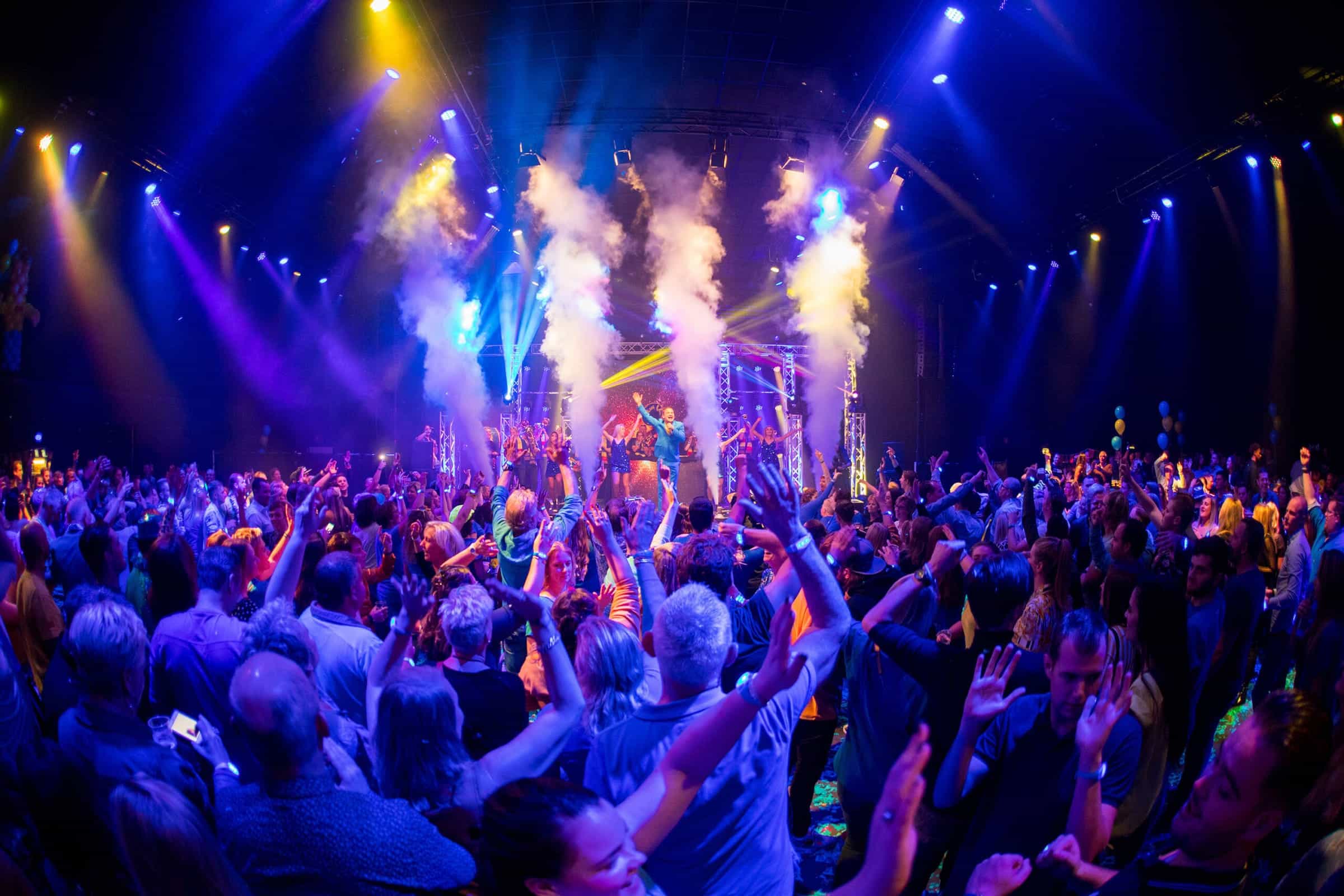 Marco Kraats op het podium voor een volle zaal, met rookkanonnen en een lichtshow
