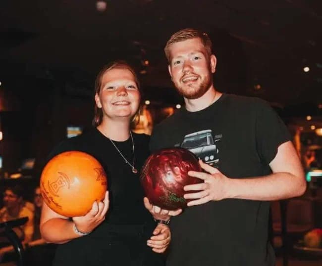 Twee gasten houden een oranje en een rode bowlingbal vast, voor de banen
