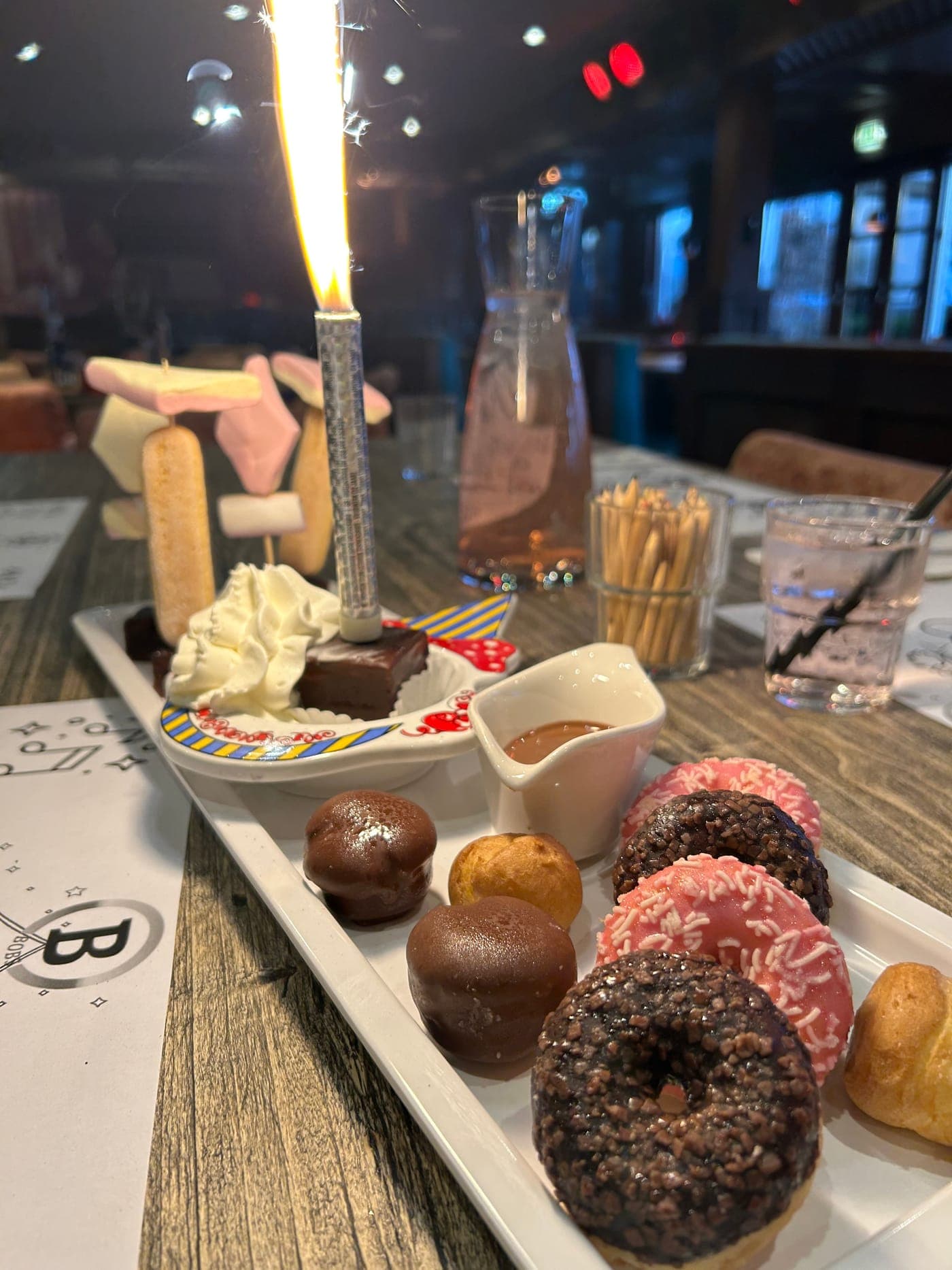 Een langwerpige schaal met donuts, soesjes en brownies, met een brandend sterretje in een stuk taart