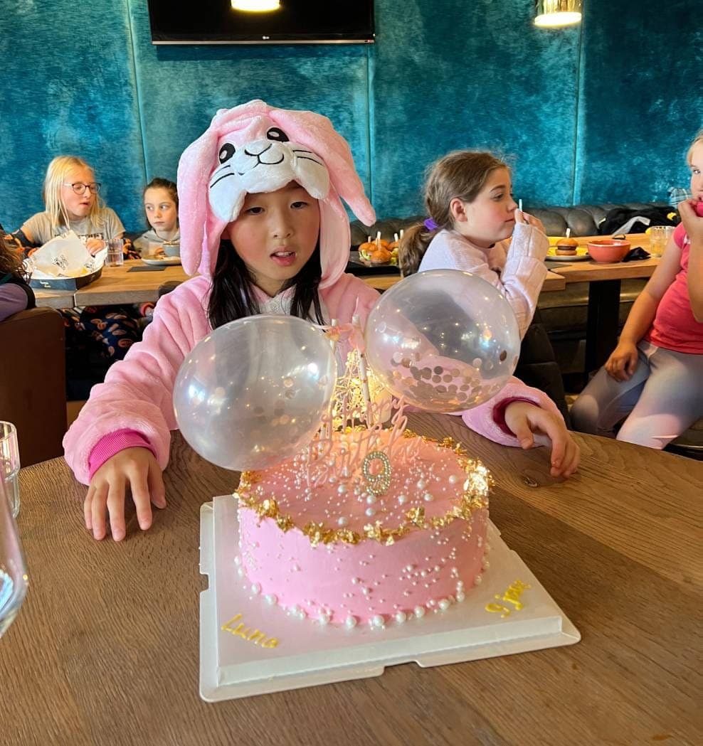 Een jarig kind achter een versierde taart met ballonnen, met vriendjes eromheen
