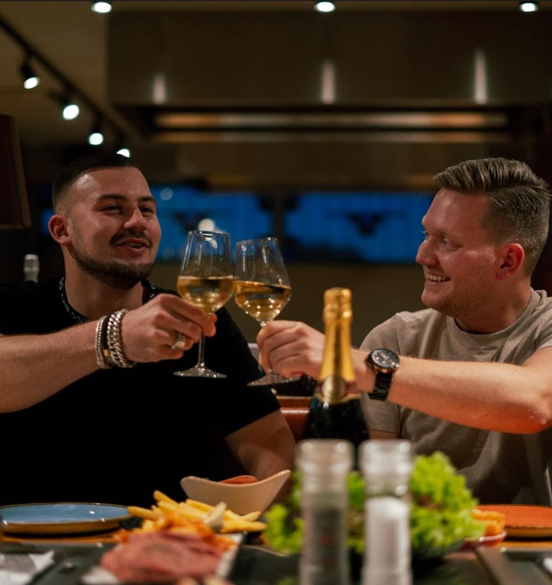 Twee gasten proosten met een glas witte wijn aan tafel
