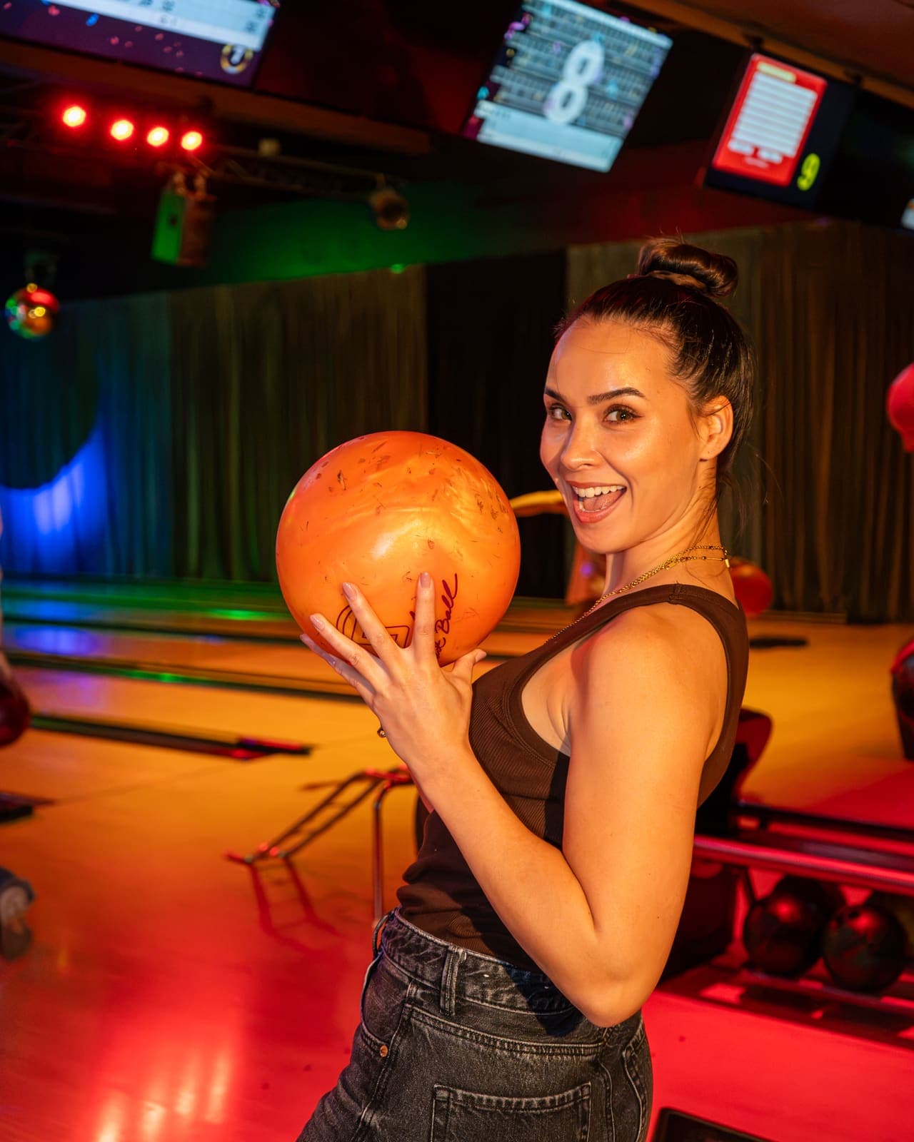 Een lachende gast houdt een oranje bowlingbal vast, voor de banen