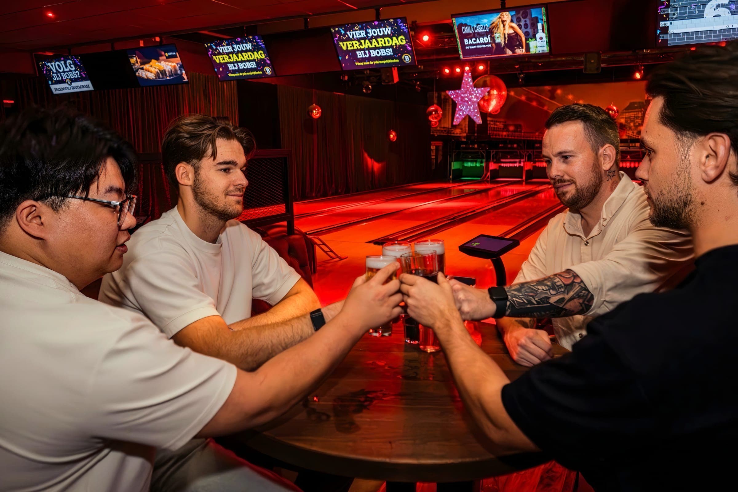 Vier vrienden proosten met bier aan een tafel naast de bowlingbanen