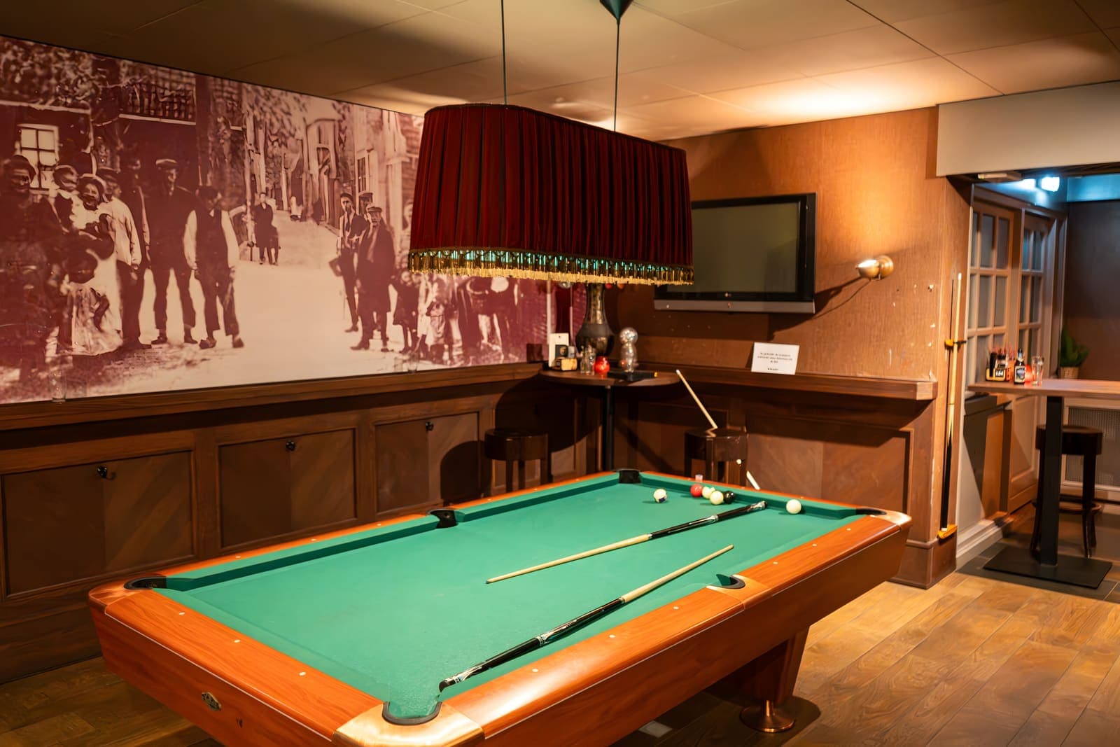 De pooltafel in het Grand Café onder een rode lamp, met een oude foto van Uitgeest op de wand