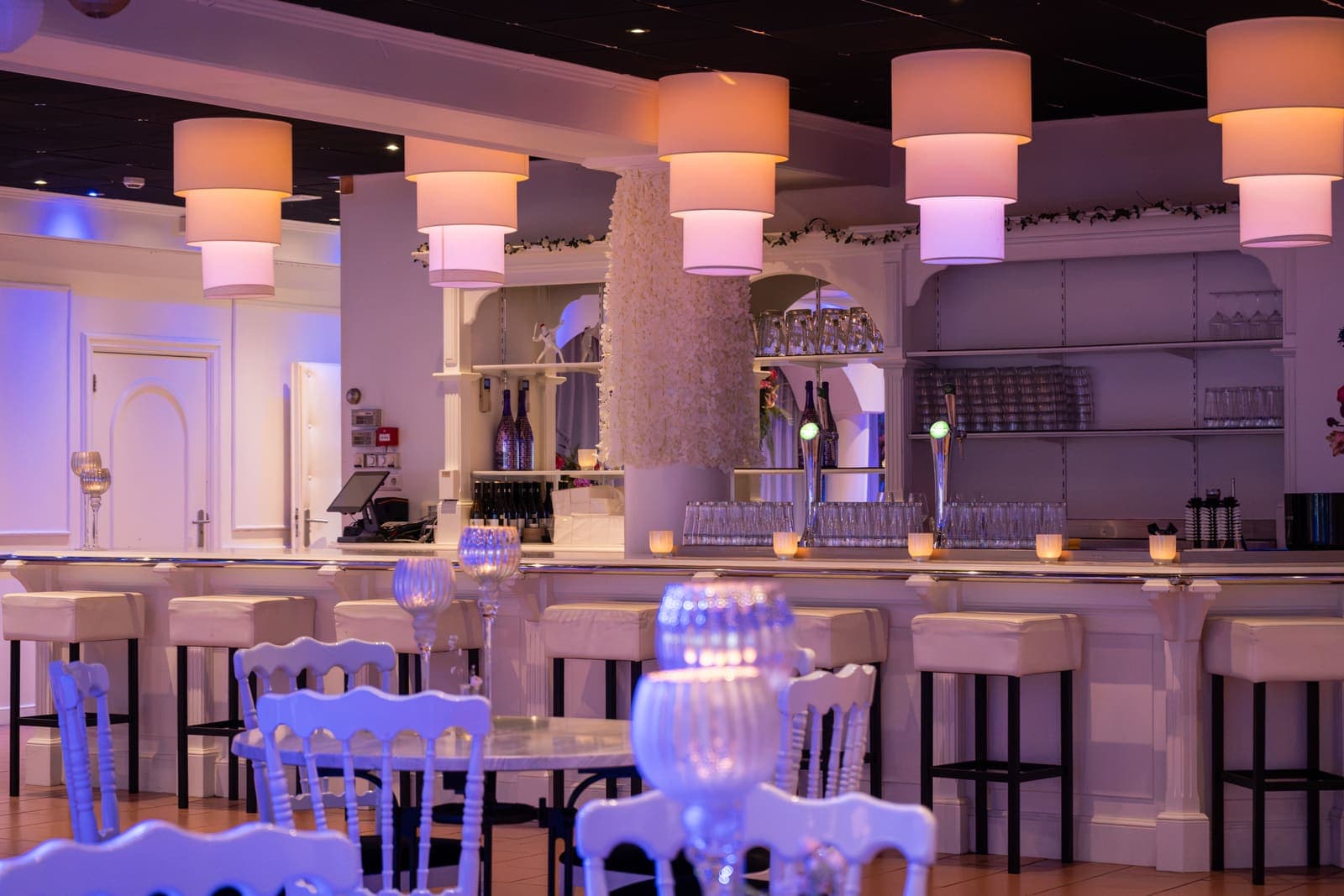 De witte bar van de South Beach Lounge met barkrukken en lampen van gelaagde kappen