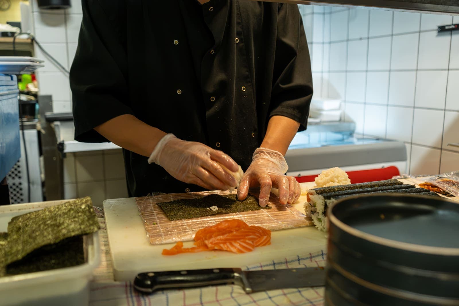 Een kok rolt sushi met zalm op een bamboematje