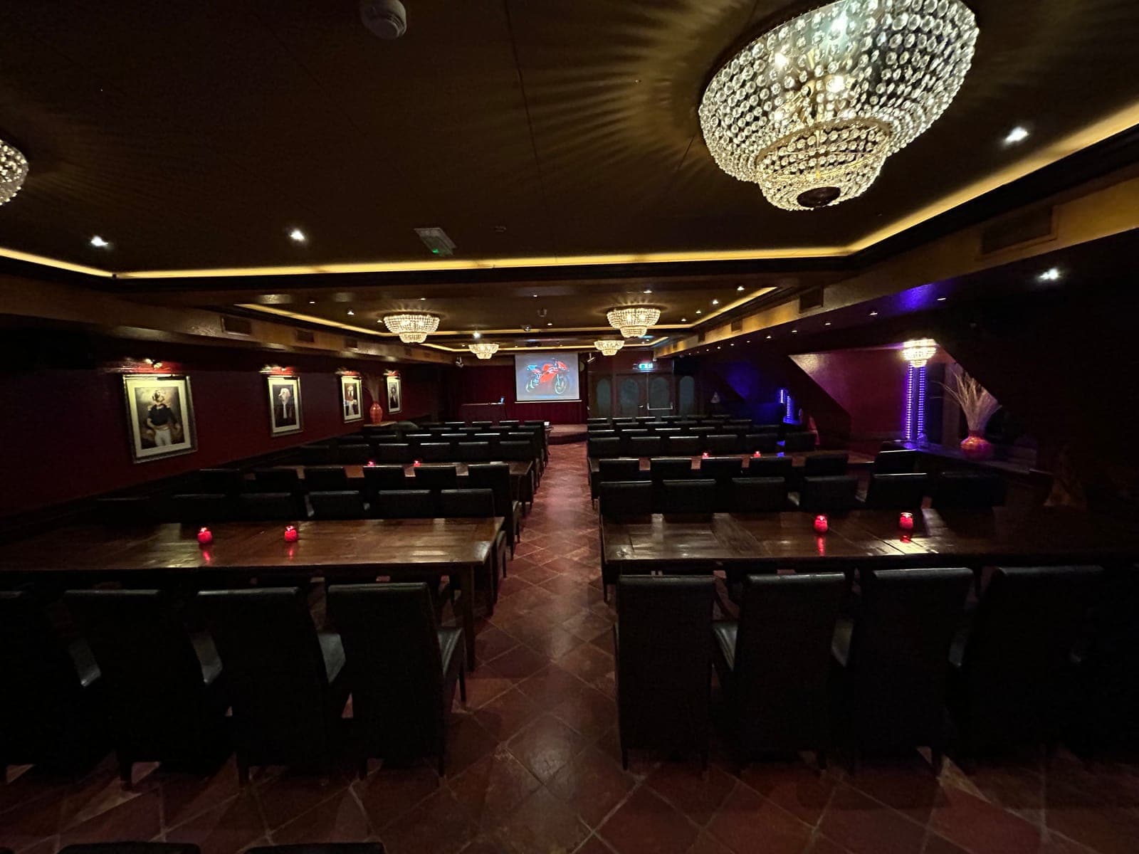 Een zaal met tafels en stoelen gericht op een groot projectiescherm