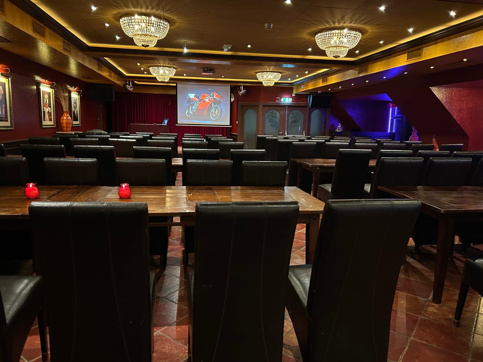 Een zaal met lange tafels tegenover elkaar, kaarsjes erop en een scherm voorin