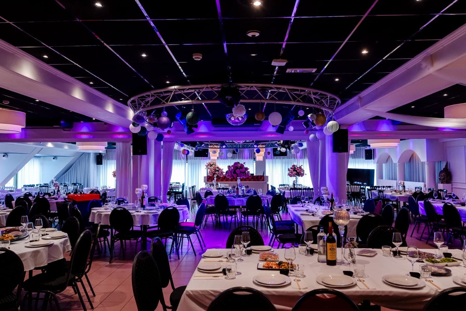 De grote zaal feestelijk aangekleed, met witte drapering, bloemstukken en gekleurd licht