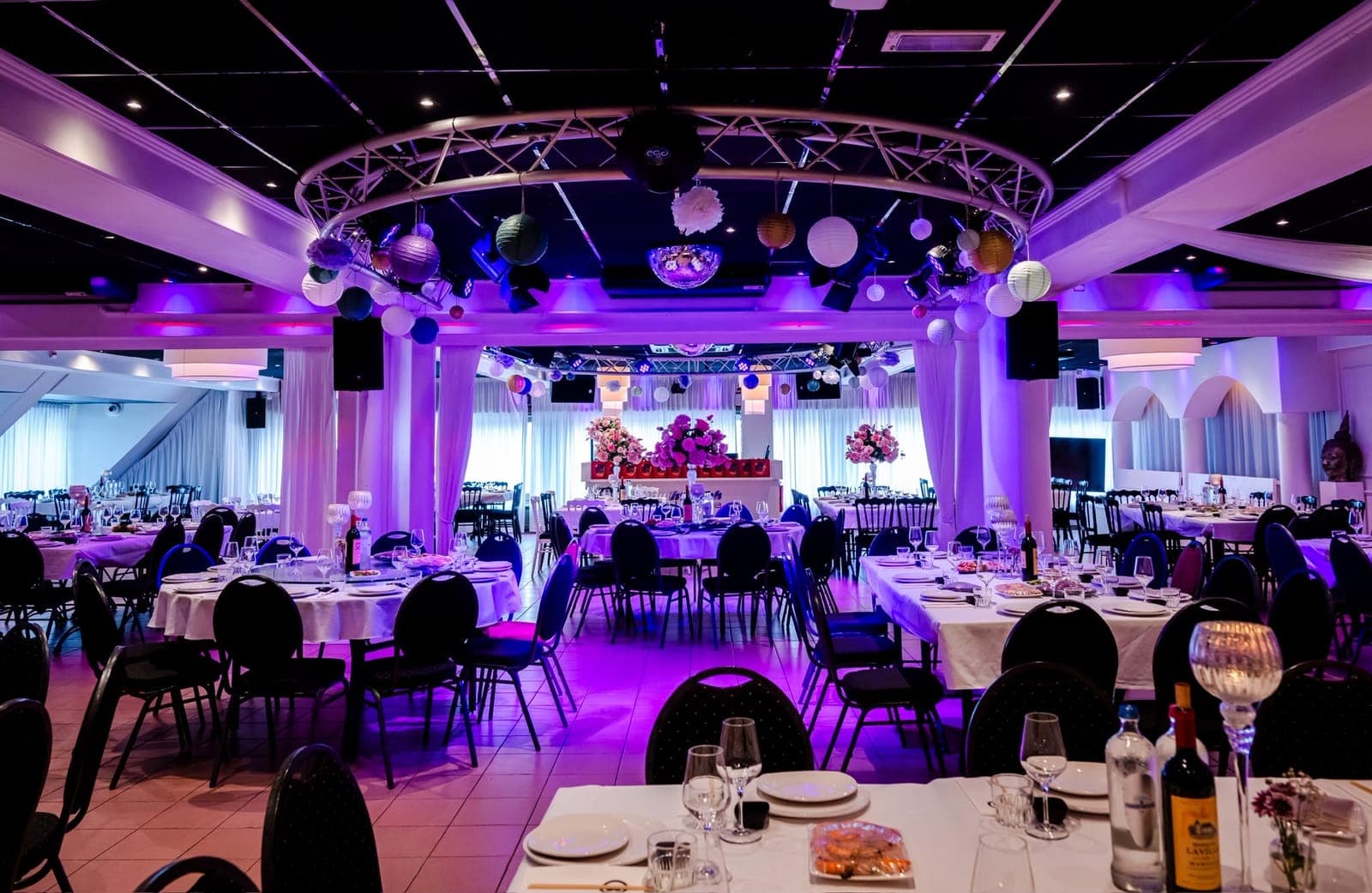 De grote zaal met ronde tafels, bloemstukken en paarse uplighting langs de wanden
