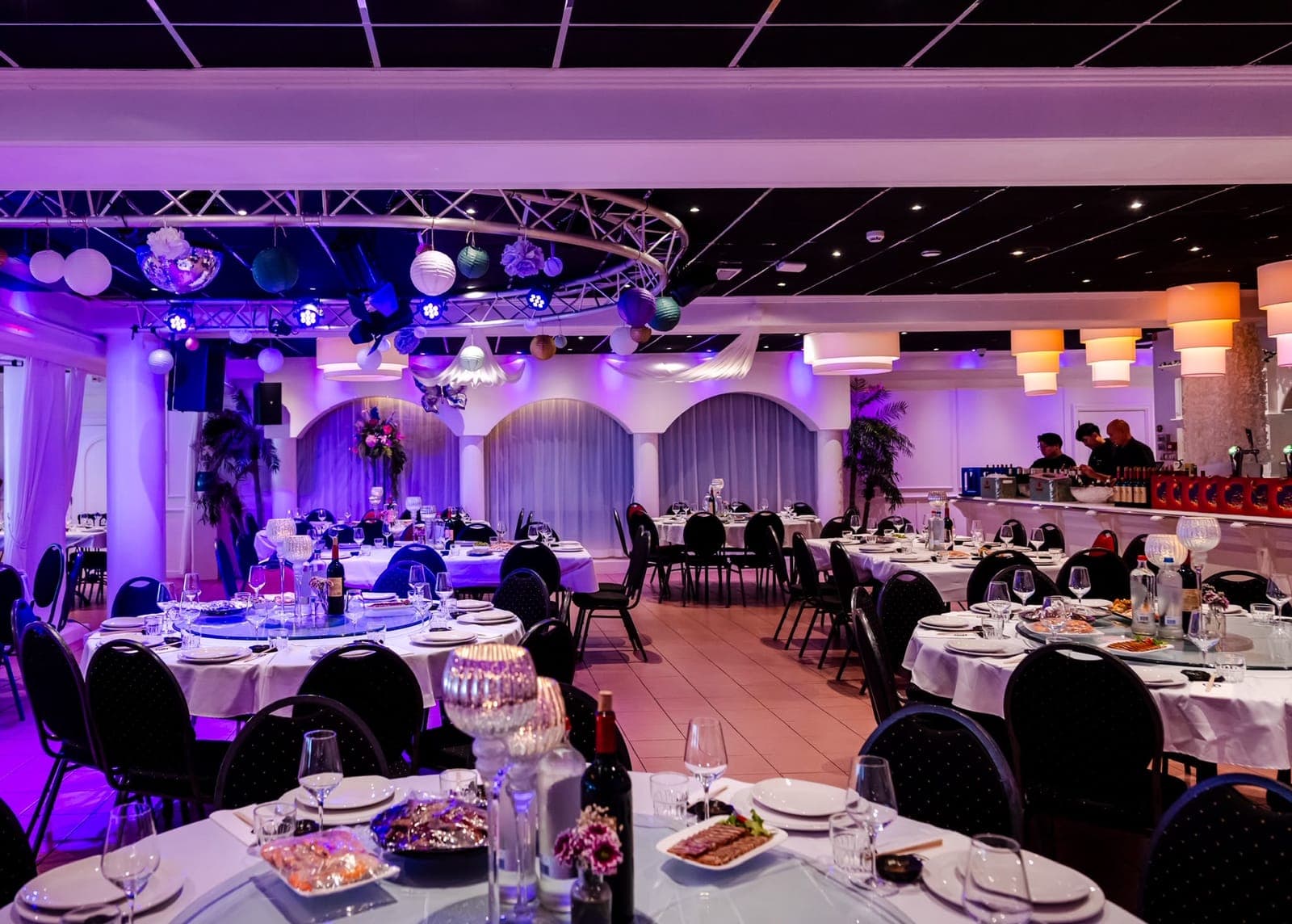 De grote zaal met open vloer, wit gedekte tafels en gekleurde uplighting
