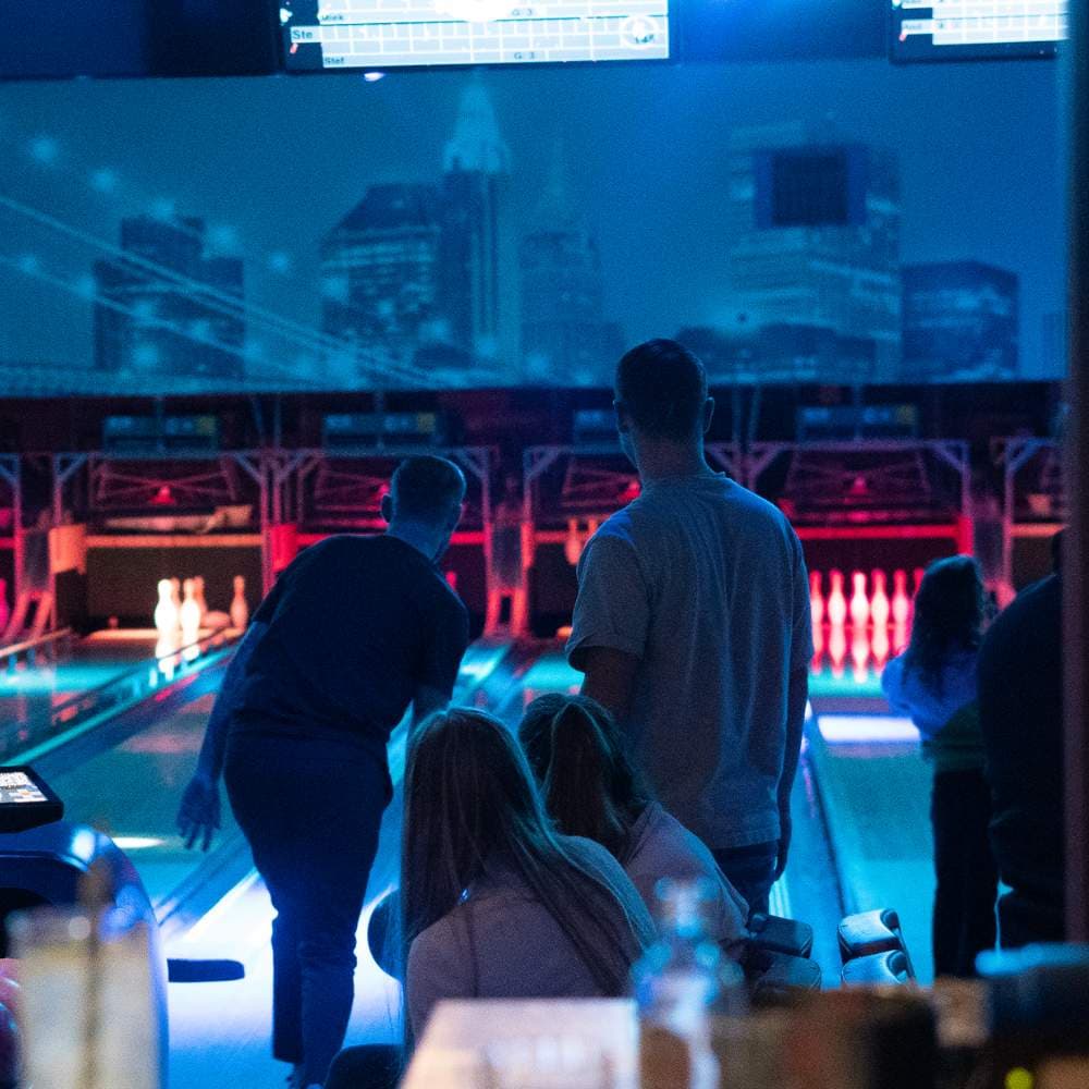 Gasten aan de baan, met de verlichte pins en het stadssilhouet op de achterwand
