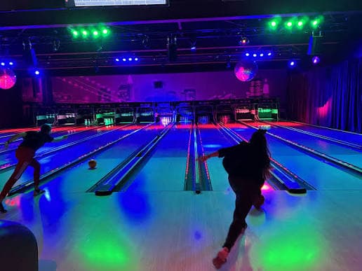 Twee gasten gooien tegelijk op de bowlingbanen, onder groene en paarse spots