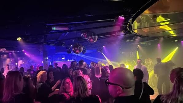 Volle dansvloer in Turbo 2000, met discobollen en gekleurde spots boven de mensen